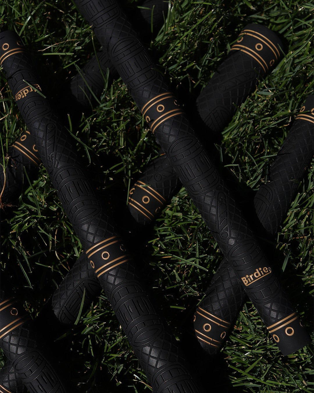 Birdie Golf Grips Smoke & Barrel black golf club grips with gold accents and raised texture, laid on green grass.