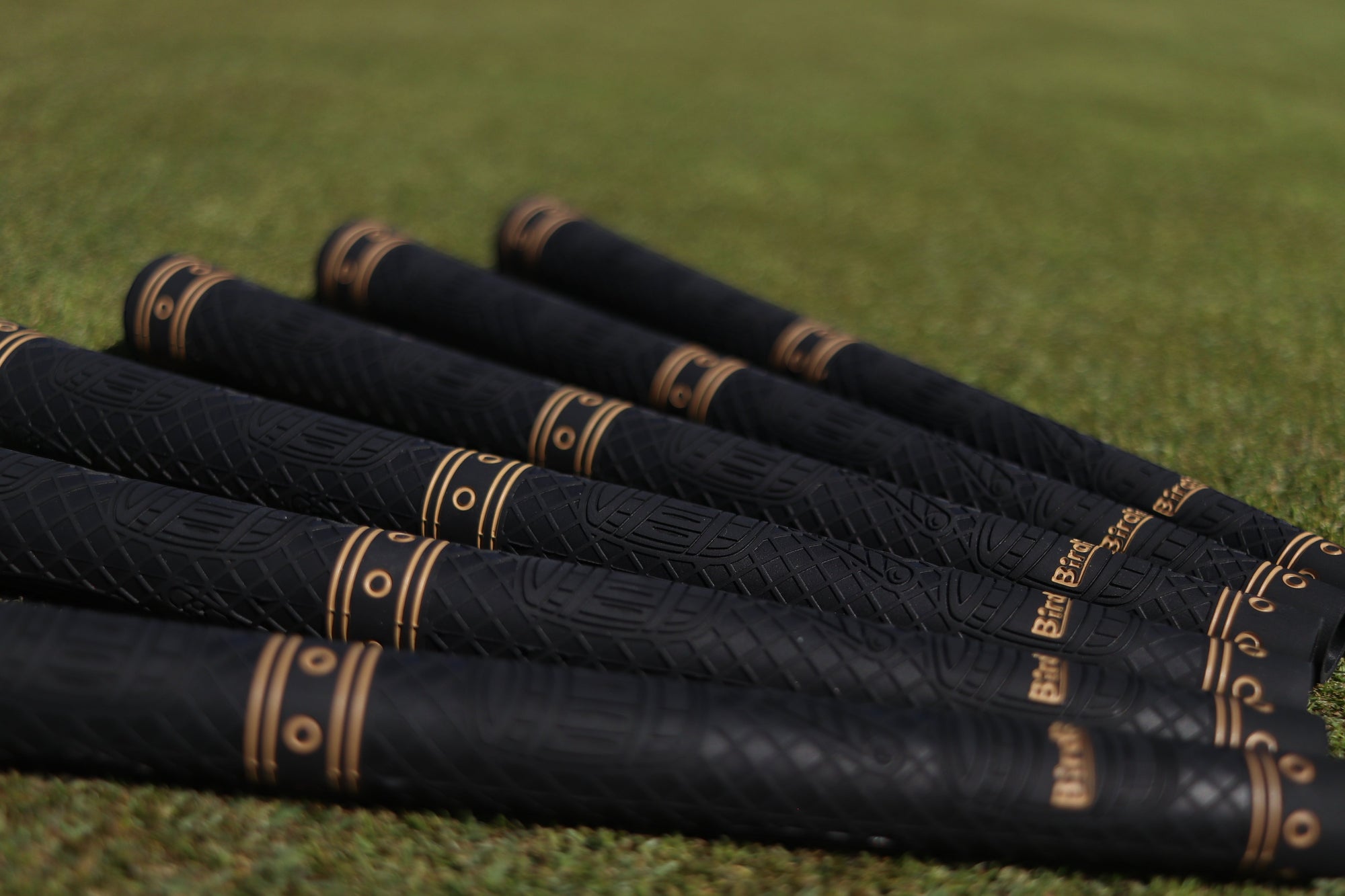 Birdie Golf Grips Smoke & Barrel black golf club grips with raised texture and gold detailing on a putting green.