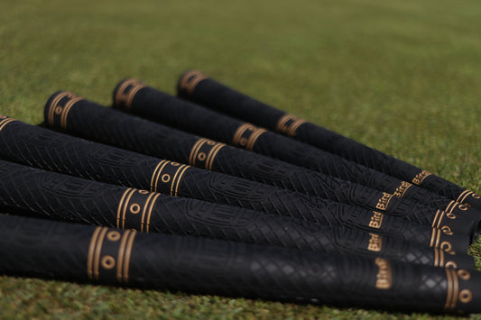 Birdie Golf Grips Smoke & Barrel black golf club grips with raised texture and gold detailing on a putting green.